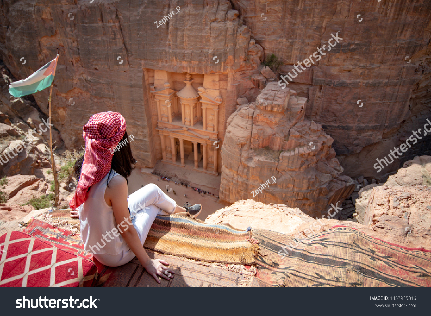 Asian woman traveler sitting on carpet viewpoint in Petra ancient city looking at the Treasury or Al-khazneh, famous travel destination of Jordan and one of seven wonders. UNESCO World Heritage site. #1457935316