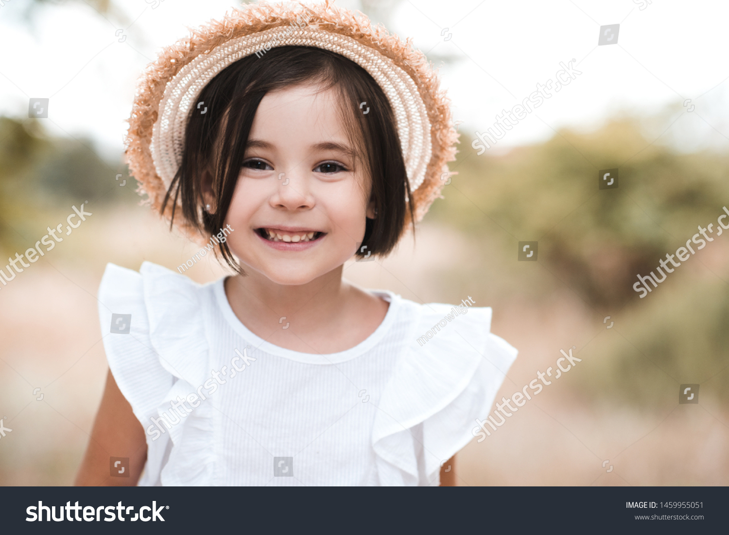 Smiling kid girl 3-4 year old wearing straw hat and white stylish shirt outdoors. Looking at camera.  #1459955051