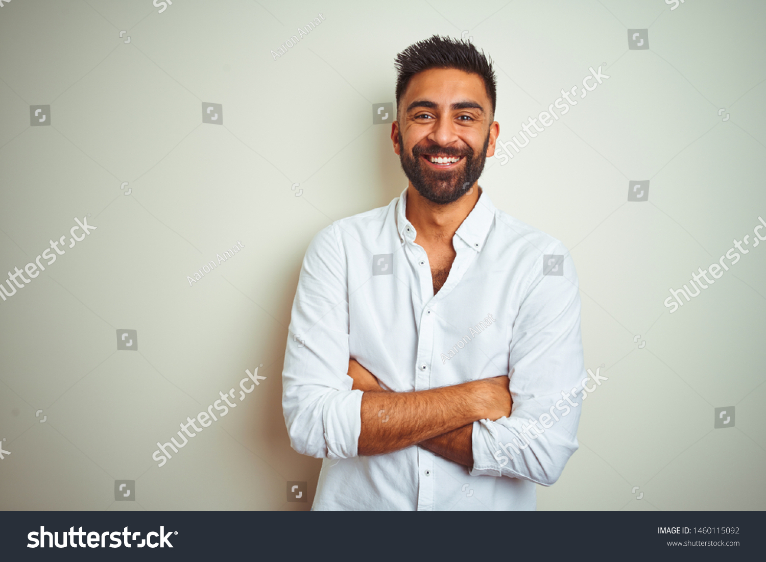 Young indian man wearing elegant shirt standing over isolated white background happy face smiling with crossed arms looking at the camera. Positive person. #1460115092