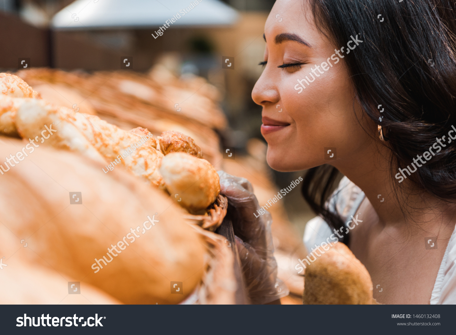 selective focus of cheerful asian woman smiling while smelling bread in supermarket  #1460132408