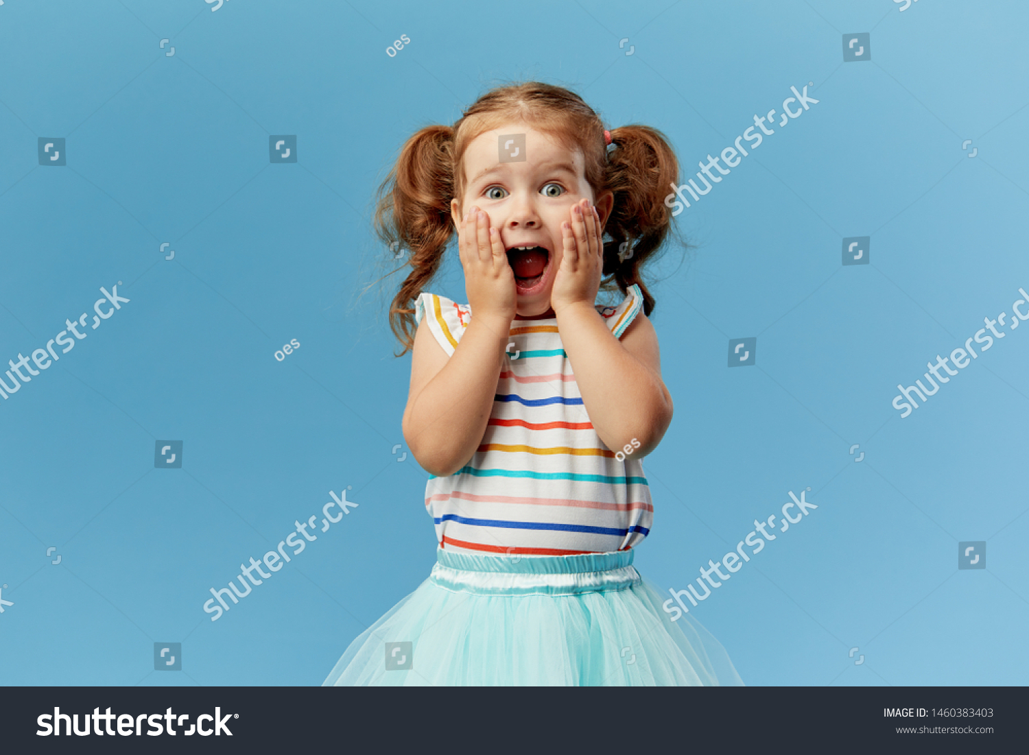 Portrait of surprised cute little toddler girl child standing isolated over blue background. Looking at camera. hands near open mouth #1460383403