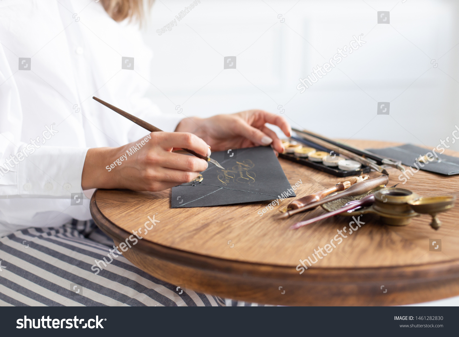 Woman calligrapher is holding a pen with ink and signs a card in handwritten font. Close-up. Soft focus. #1461282830