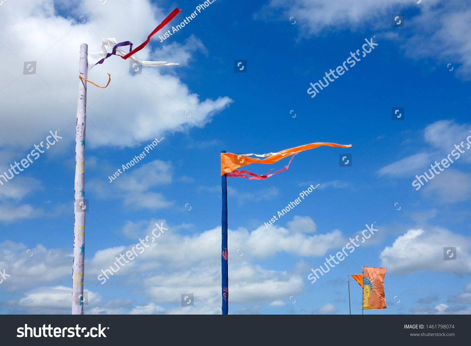 Brightly coloured orange flags wave against a bright blue sky with clouds.  Image has copy space. #1461798074