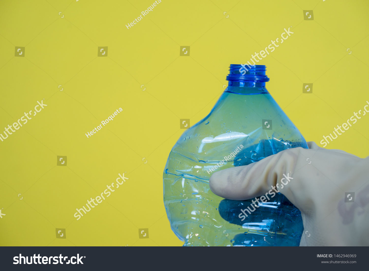blue plastic bottle held in hand with gloves, yellow background #1462946969