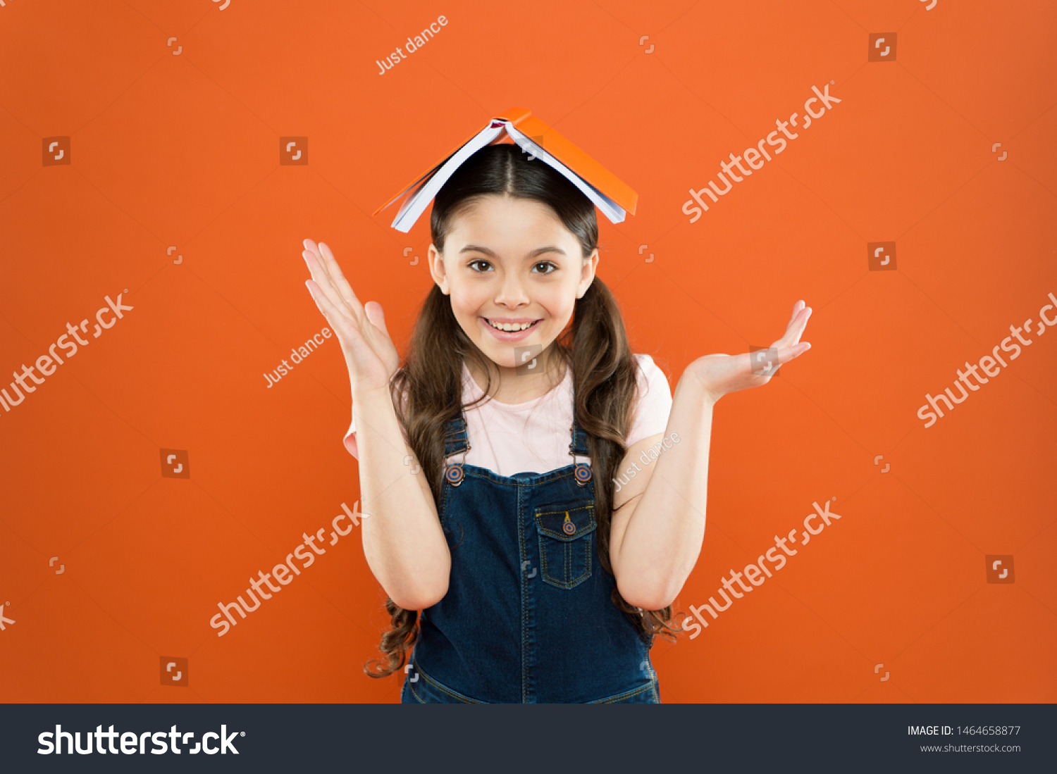 Interesting story for kid. Studying and relaxing. Study at home. Homework concept. Homeschooling and private lesson. Book on her head. Little girl book roof head. Small girl book orange background. #1464658877