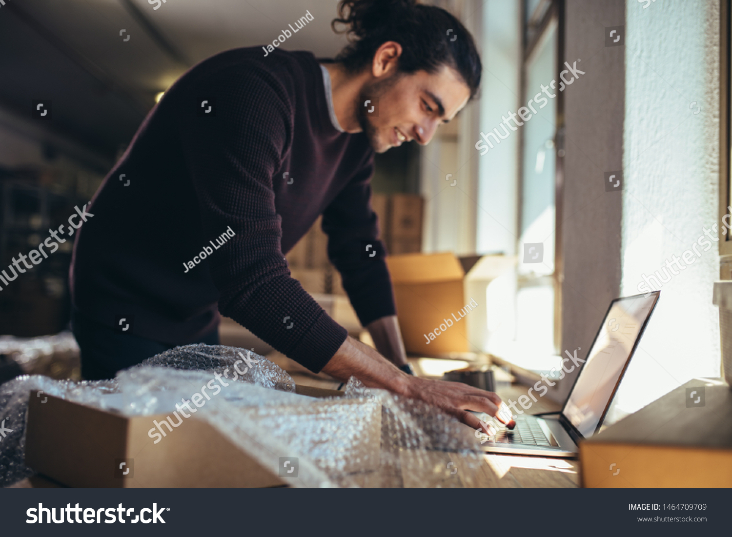 Young man working on laptop with parcel on the side. Drop shipping business owner updating the delivery status of the shipment. #1464709709