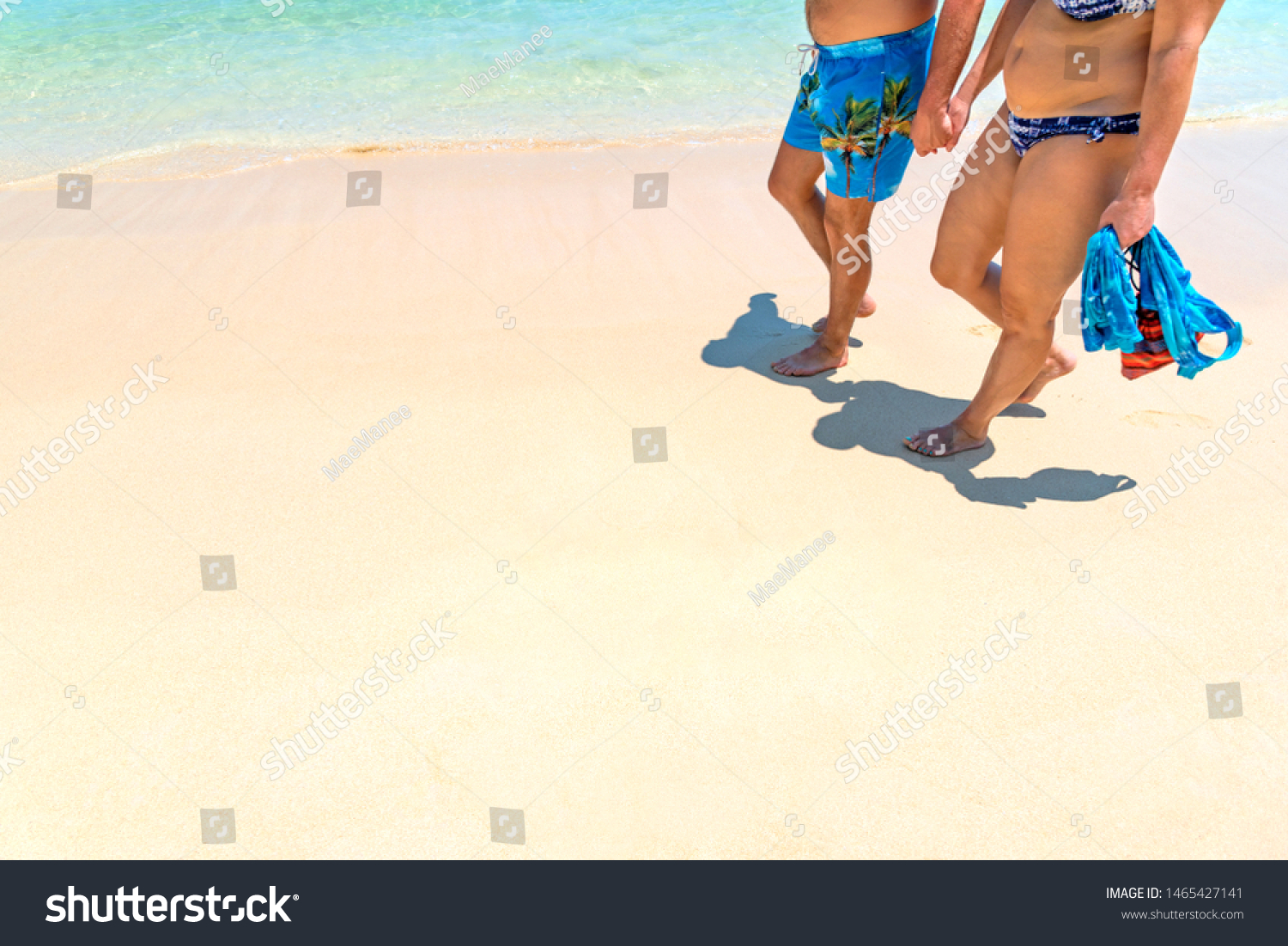 Close up of senior couple in swim suit walking on golden sand beach in summer season. Happy romantic Caucasian man and woman hand in hand enjoy vacation. Travel vacation retirement lifestyle concept. #1465427141