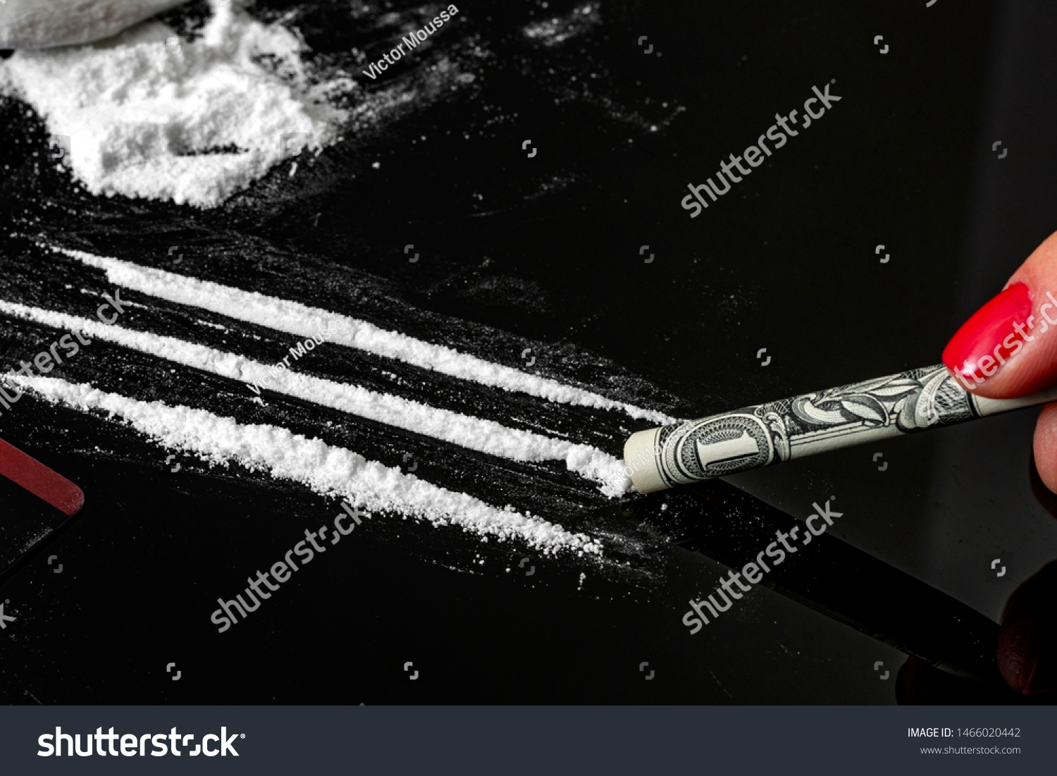 Drug addiction and substance abuse concept theme with close up on a troubled addict using a one dollar bill as a straw to snort a line of cocaine on a dark mirror table next to a pile of white powder #1466020442