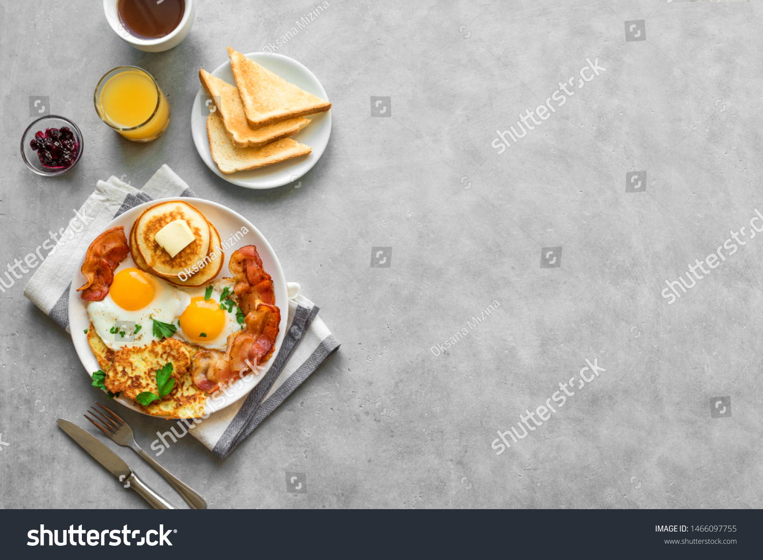 Full American Breakfast on gray, top view, copy space. Sunny side fried eggs, roasted bacon, hash brown, pancakes, toasts, orange juice and coffee for breakfast. #1466097755
