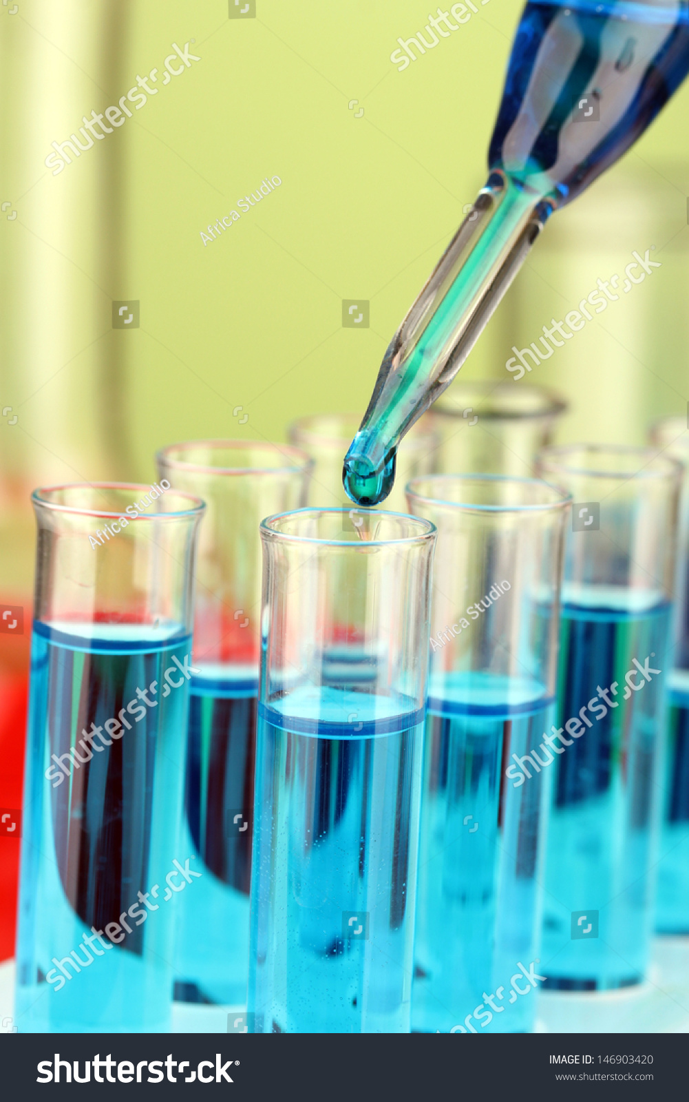 Laboratory pipette with drop of color liquid over glass test tubes, close up #146903420