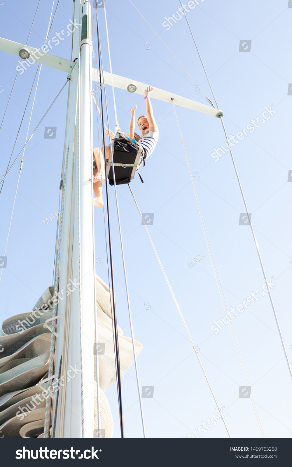 Brother and sister together high up climbing mast on luxury sailing yacht, joyful expressions against sunny blue sky, outdoors. Family summer adventure, boat activities leisure recreation lifestyle. #1469753258
