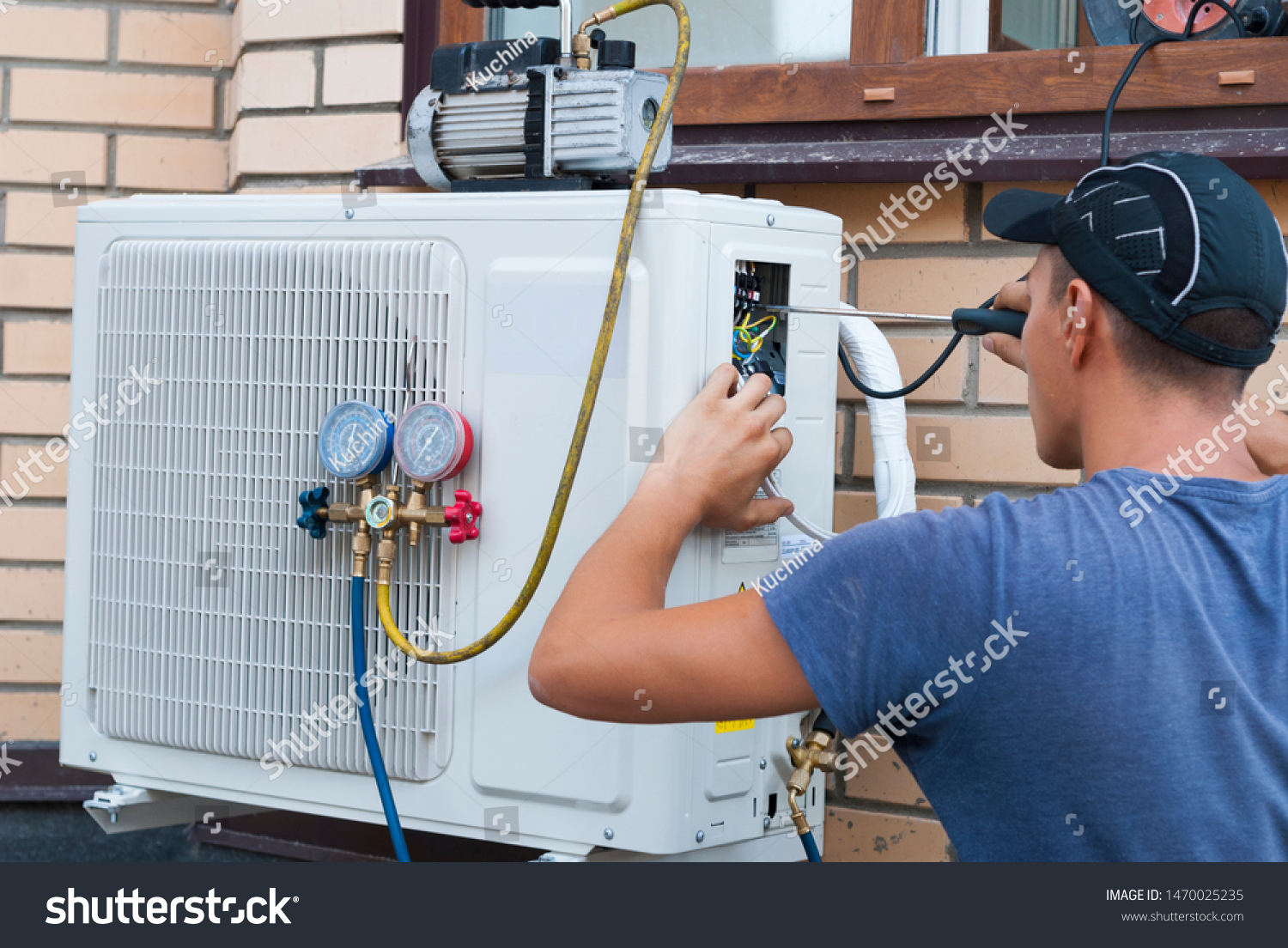 the worker installs the outdoor unit of the air conditioner on the wall of the house #1470025235