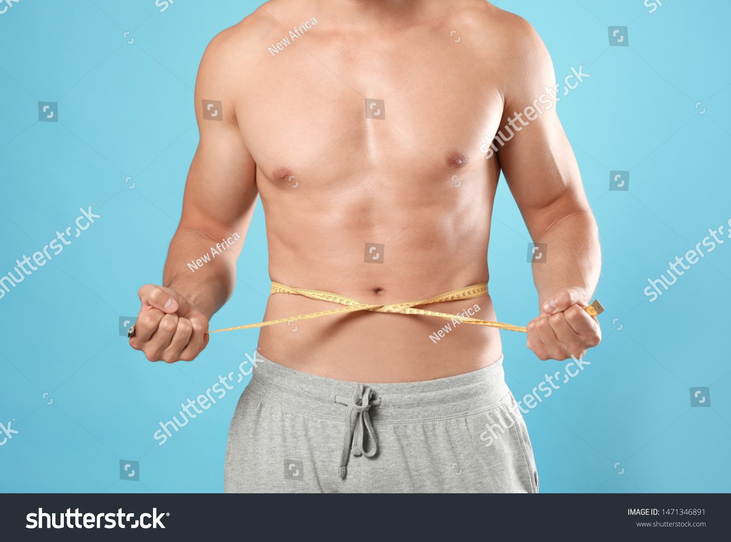 Young man with slim body using measuring tape on light blue background, closeup view #1471346891