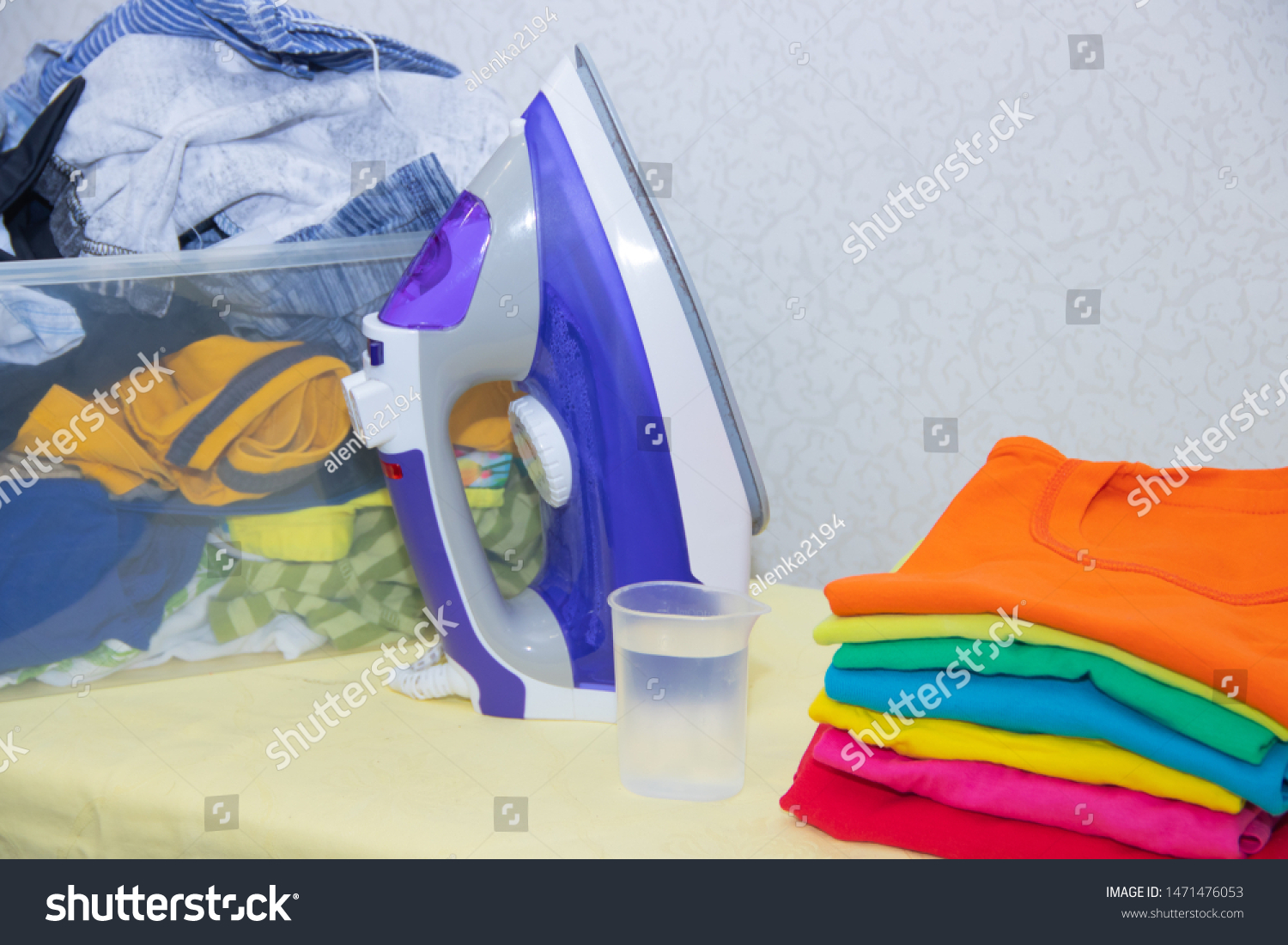 Iron and baby clothes. Colored clothes on an ironing board. Bright t-shirts. Ironed and non-ironed colored children's underwear on the board. Ironing board. A pile of things. #1471476053