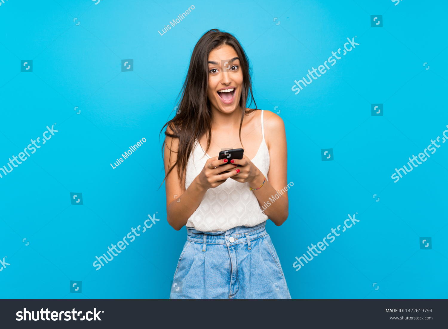 Young woman over isolated blue background surprised and sending a message #1472619794