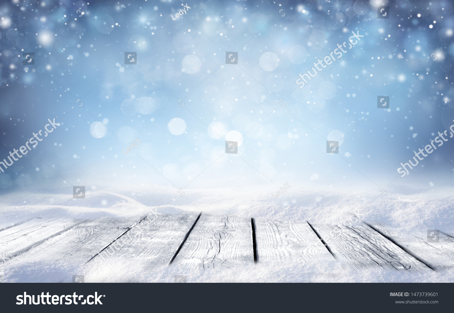 Beautiful winter snowy blurred defocused blue background and empty wooden flooring. Flakes of snow fall and sparkle on light, copy space. #1473739601