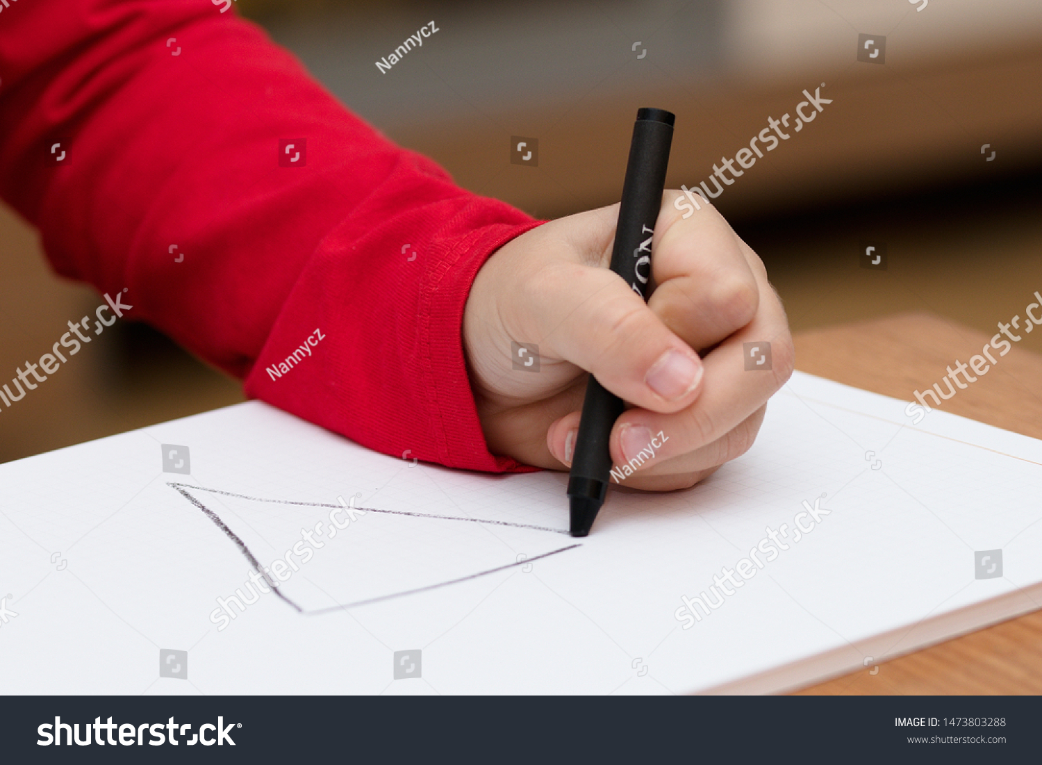Left hand of a child drawing on white paper using black crayon #1473803288