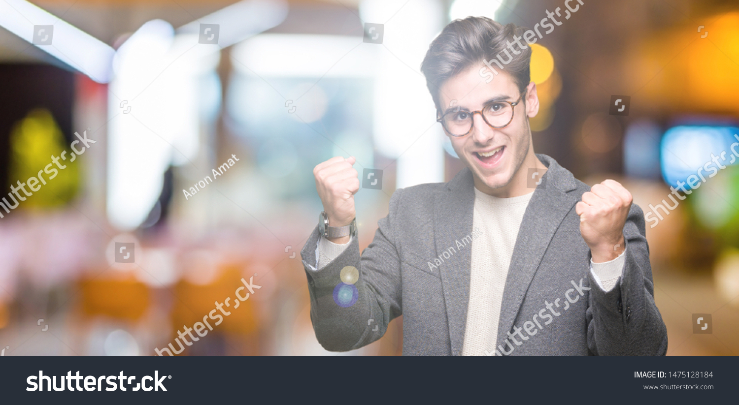 Young business man wearing glasses over isolated background celebrating surprised and amazed for success with arms raised and open eyes. Winner concept. #1475128184