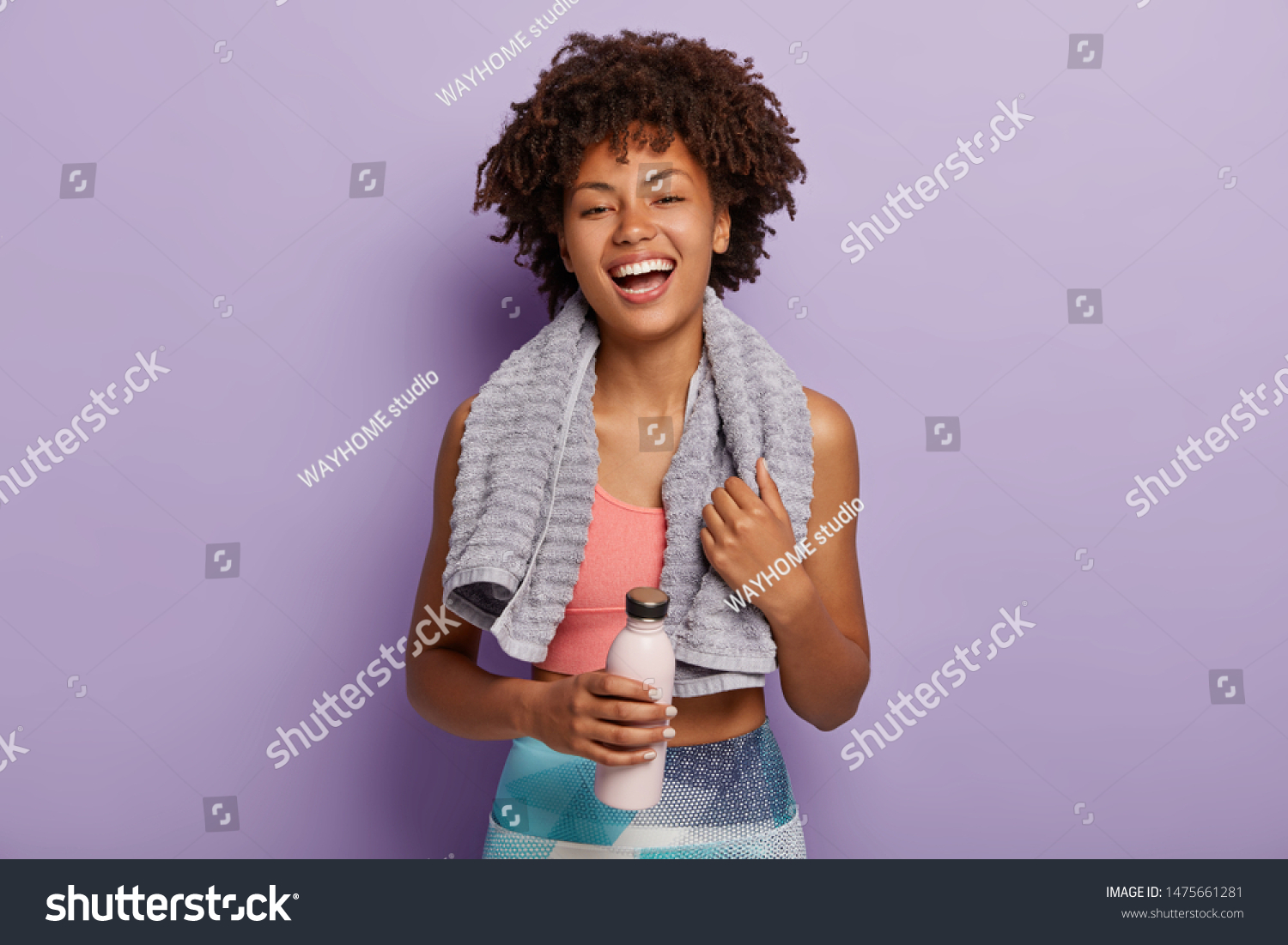 Smiling fitness woman in top and leggings takes break after training, holds bottle of water, wipes sweat with towel, being energetic runner or jogger, feels thirsty. People, wellness, vitality concept #1475661281