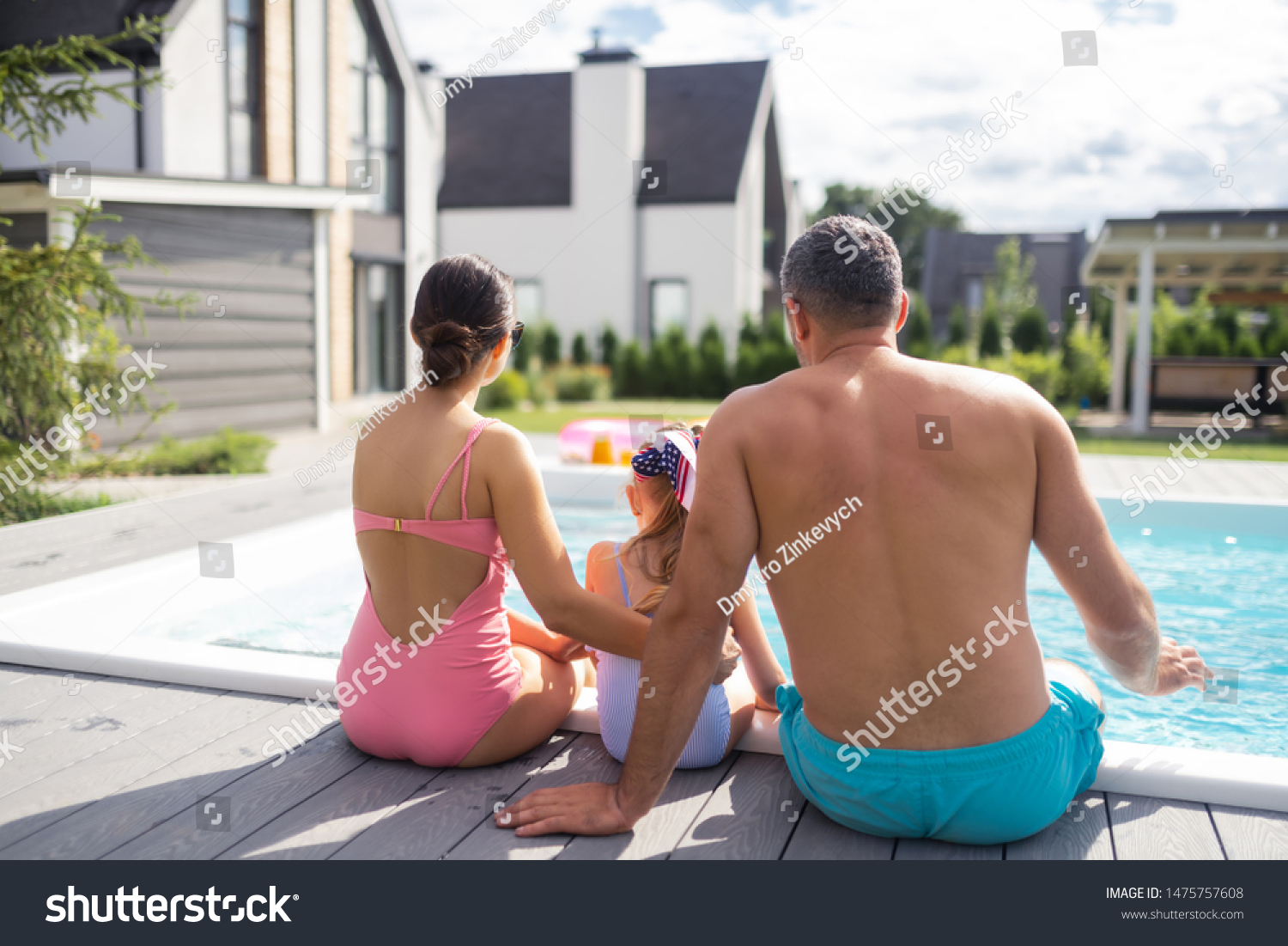 Pool near house. Happy family wearing swimsuits sitting near pool near their private house #1475757608