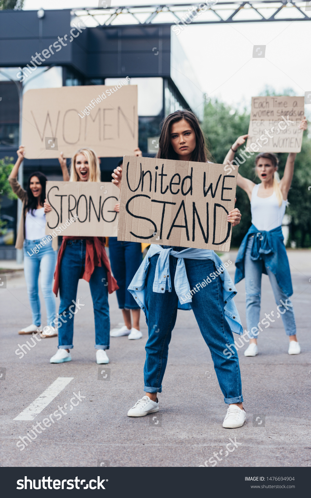 full length view of feminist holding placard with inscription united we stand near women on street #1476694904