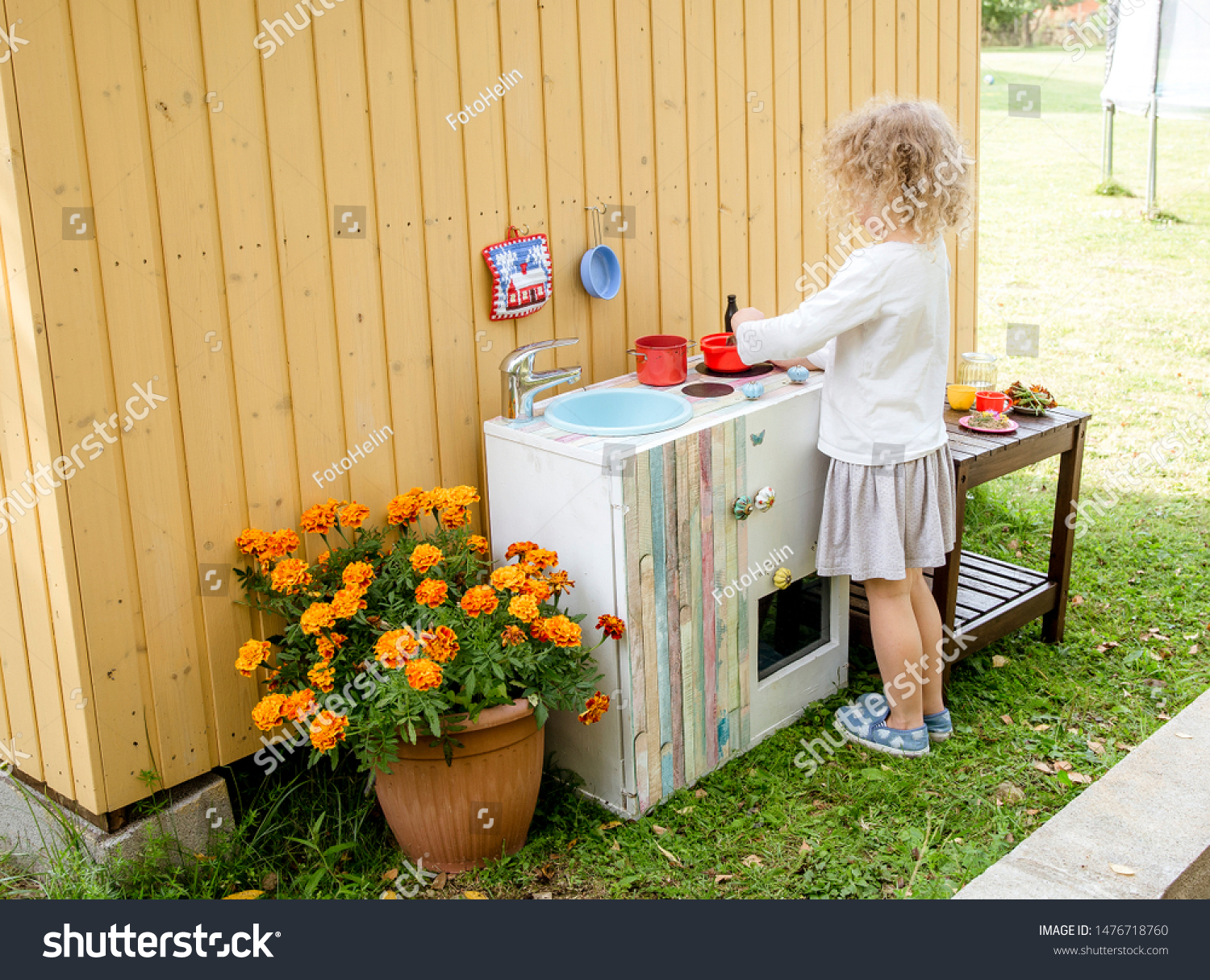 Young girl child playing outdoors in so called mud kitchen, where you can make fake food, play with sand, dirt, water, plants and make a mess, it develops imagination and exploration. #1476718760