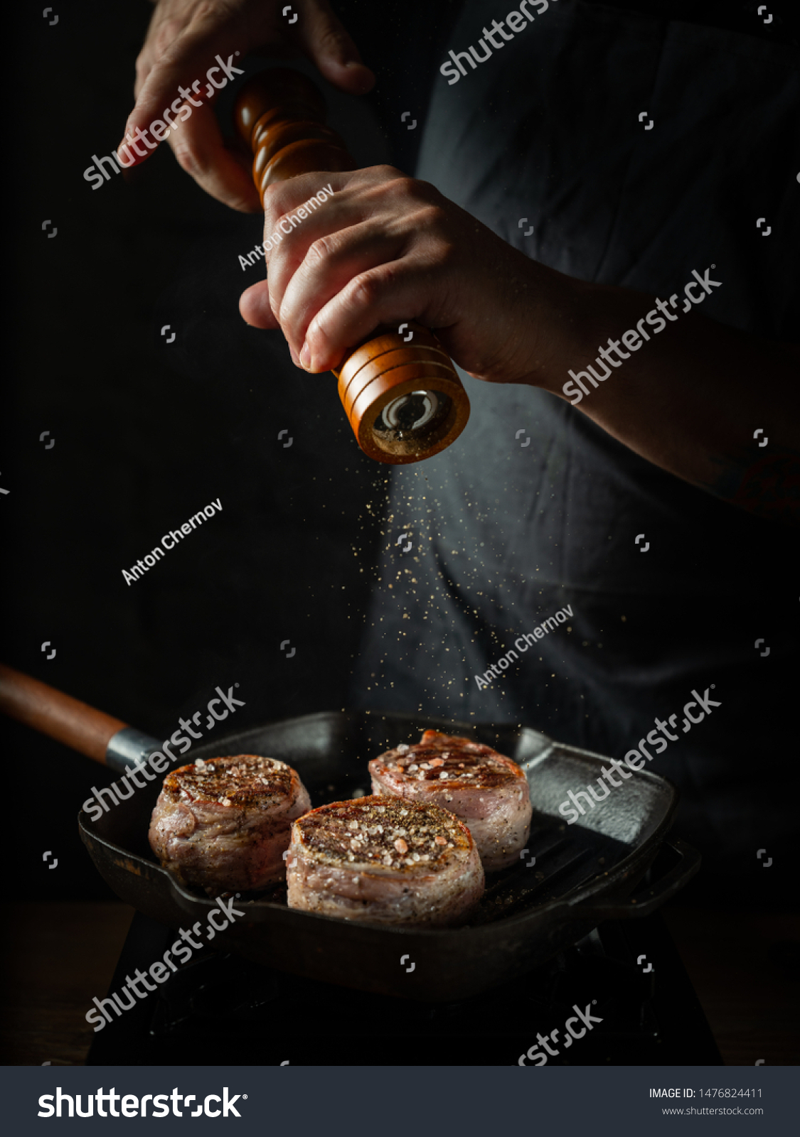Close up chef hands adding pepper in mill during cooking beef steak on grill pan black background for copy space text restaurant menu, #1476824411