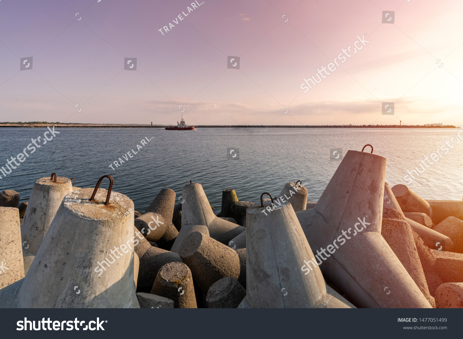 Ship-tugboat goes in high seas to tow cargo ship to port. Beautiful sunset over the pier. Tetrapod breakwaters in harbor. #1477051499