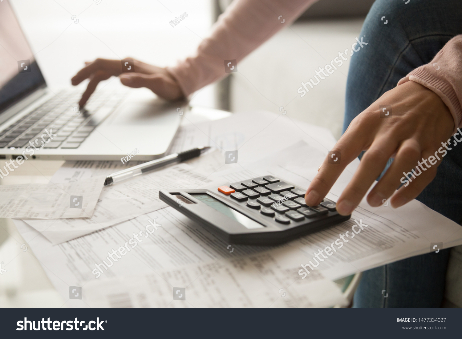 Close up cropped image young woman calculating monthly expenses, managing budget, entering data in computer application, sitting at table full of papers, loan documents, invoices, utility bills. #1477334027