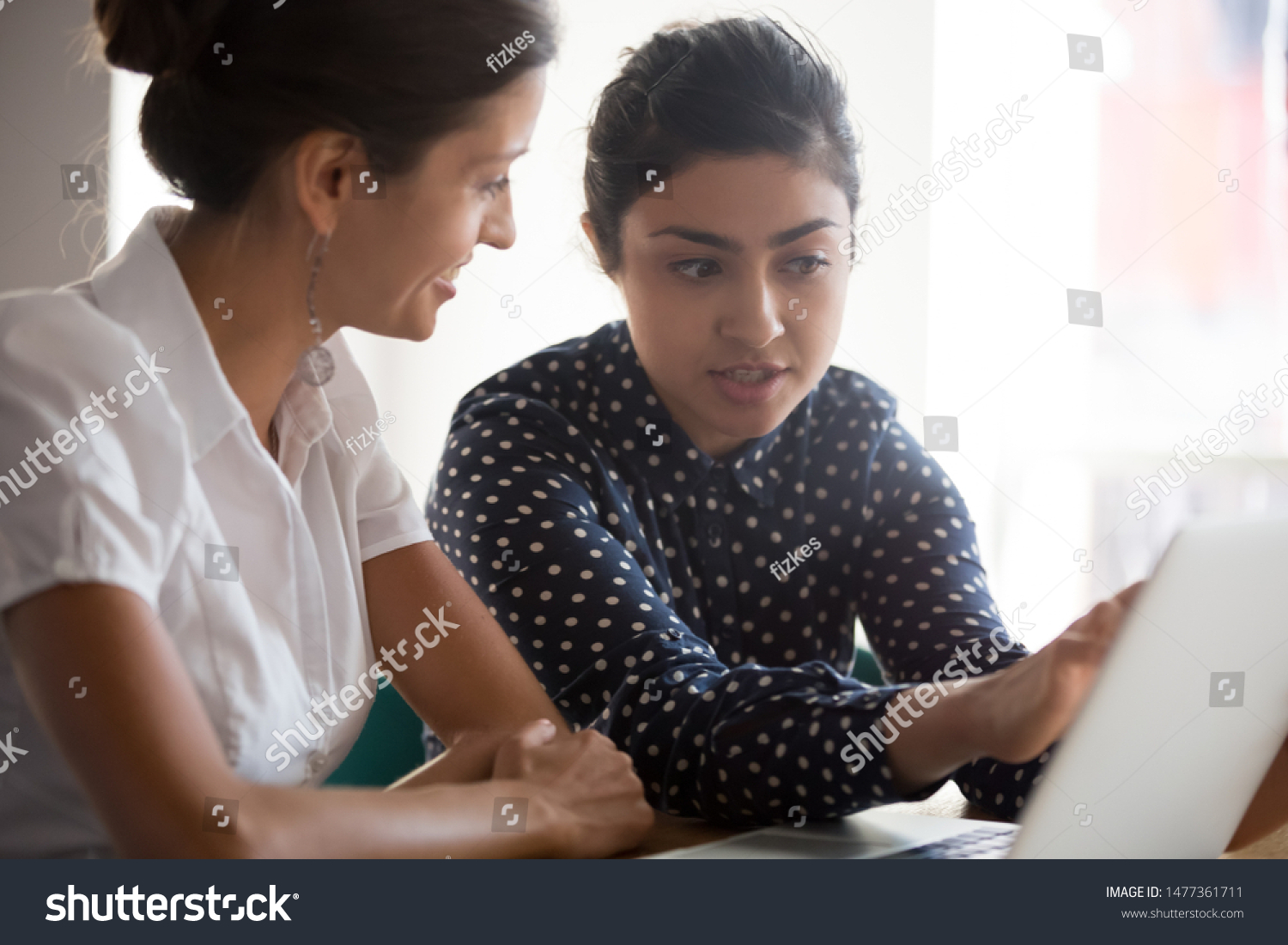 Diverse businesswomen discuss analyse online project look at laptop screen colleagues brainstorming strategizing together, mentor helping apprentice explain corporate program, support teamwork concept #1477361711