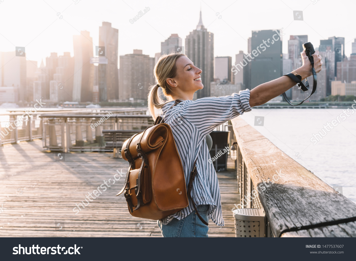 Side view of cheerful woman traveller with touristic backpack enjoying American getaway posing for clicking selfie picture with retro instant camera, concept of happiness and vacations #1477537607