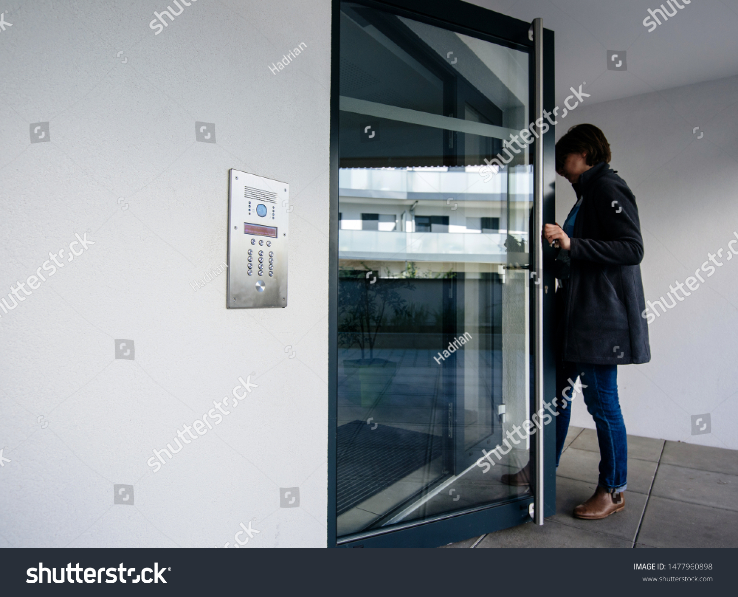 Side view of woman entering modern apartment building with glass door and modern intercom system #1477960898