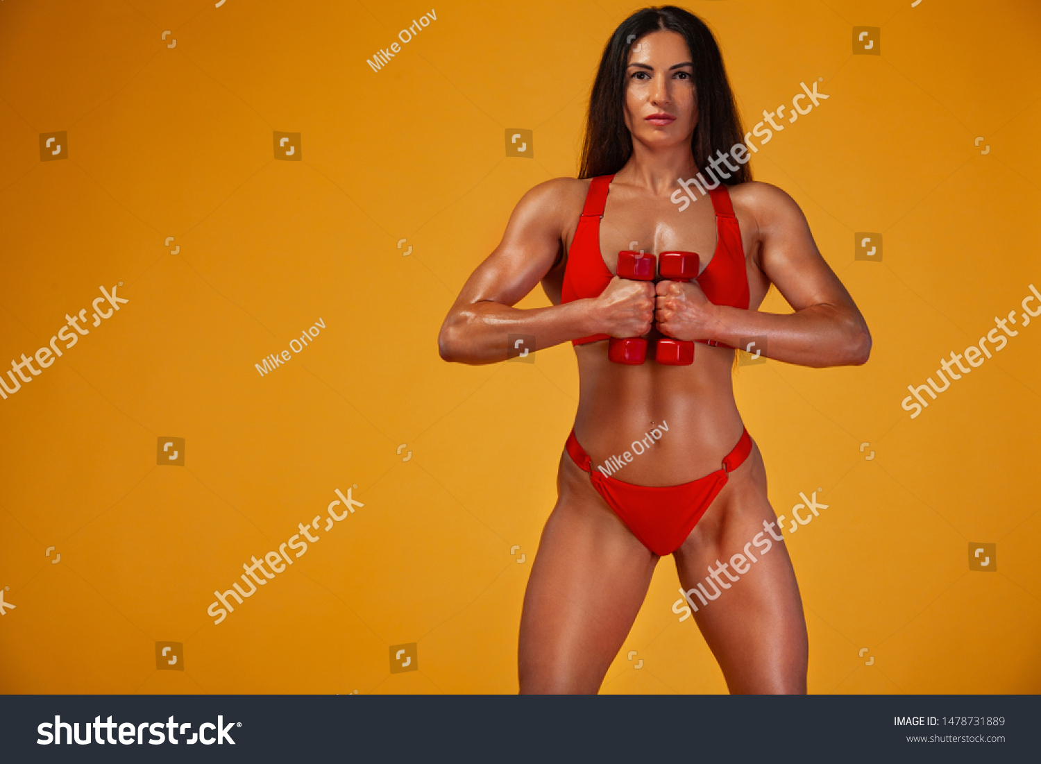 Strong muscular bodybuilder athletic woman pumping up muscles with dumbbells on yellow background. Individual sports recreation. #1478731889