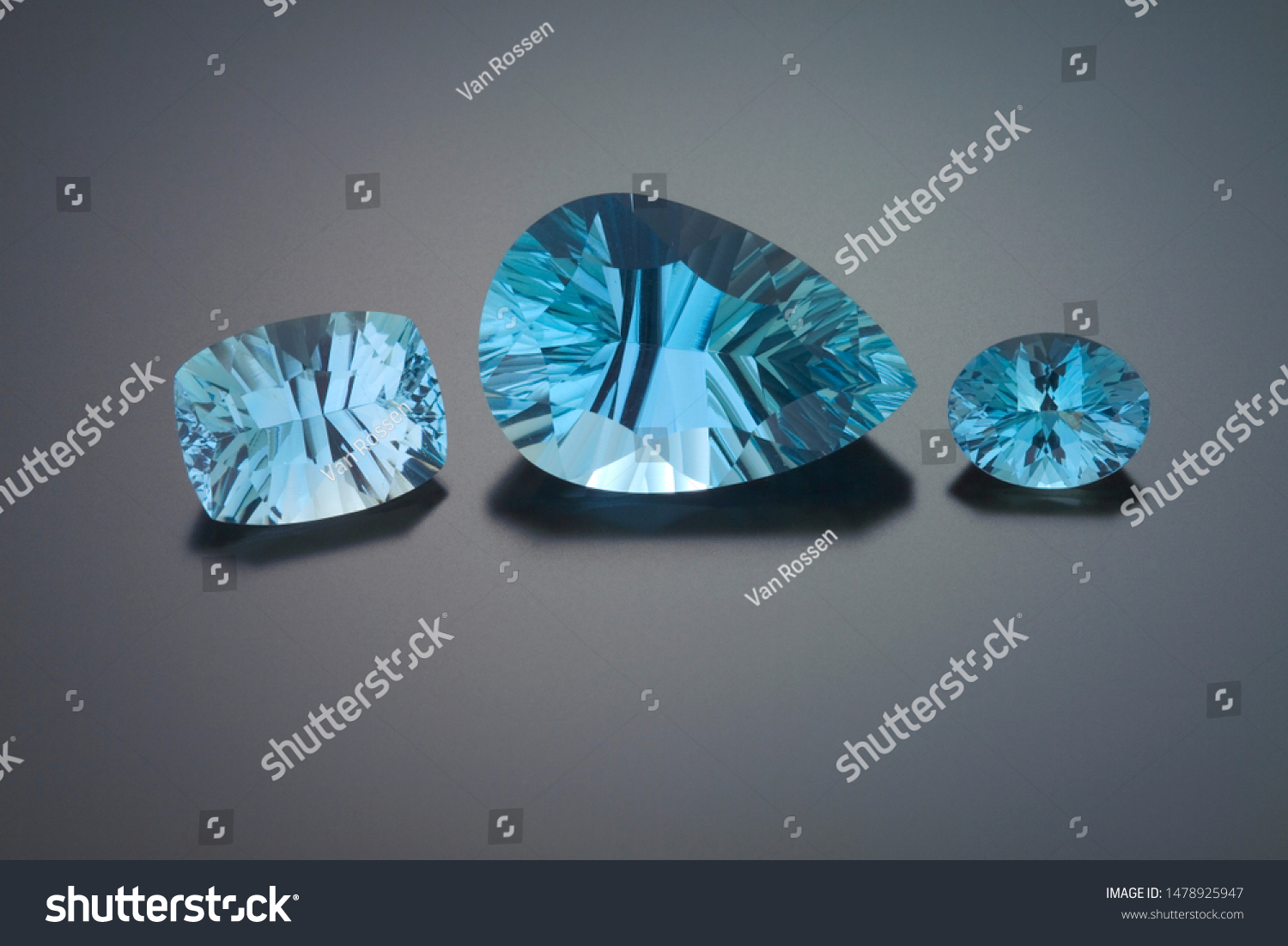 A pincushion rectangles, a large pear and an oval shape faceted aquamarine are shown on a grey reflective background. #1478925947
