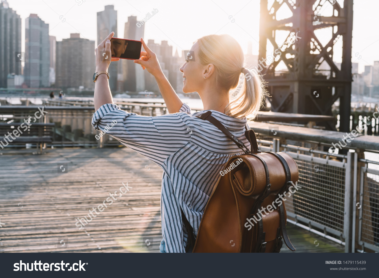 Back view of millennial woman shooting video of New York landscape using smartphone for clicking pictures, positive female tourist testing cellphone camera for taking photos of city in sunrise #1479115439