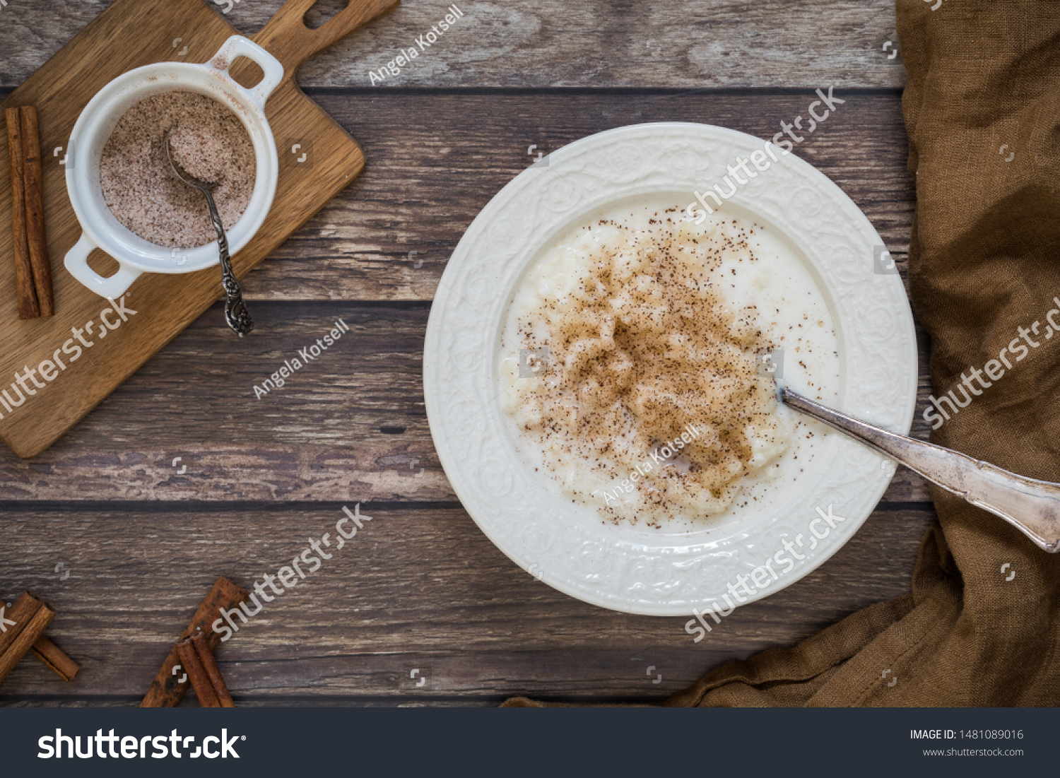 Traditional Swedish rice pudding with ground cinnamon flat lay from above perspective. There is a small bowl with cinnamon and sugar on a wooden chopping board next to the food. #1481089016