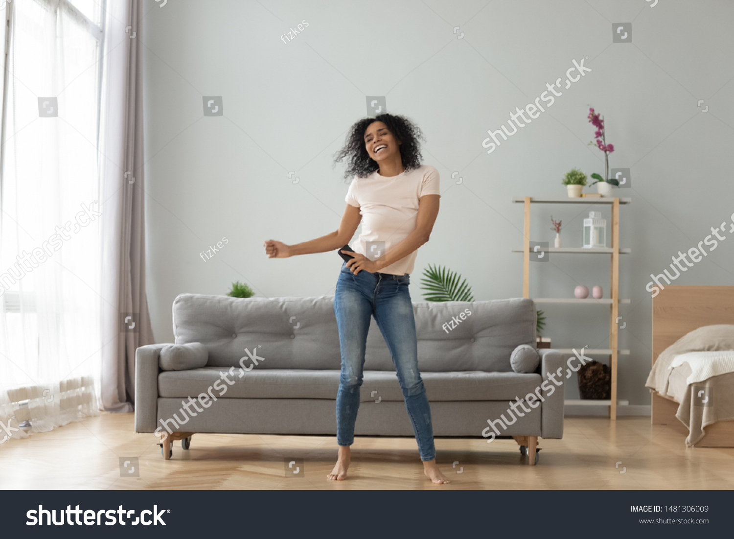 Overjoyed black biracial millennial girl dancing alone moving to rhythm in living room, happy african American young woman have fun enjoying listening to music, entertain on weekend at home #1481306009