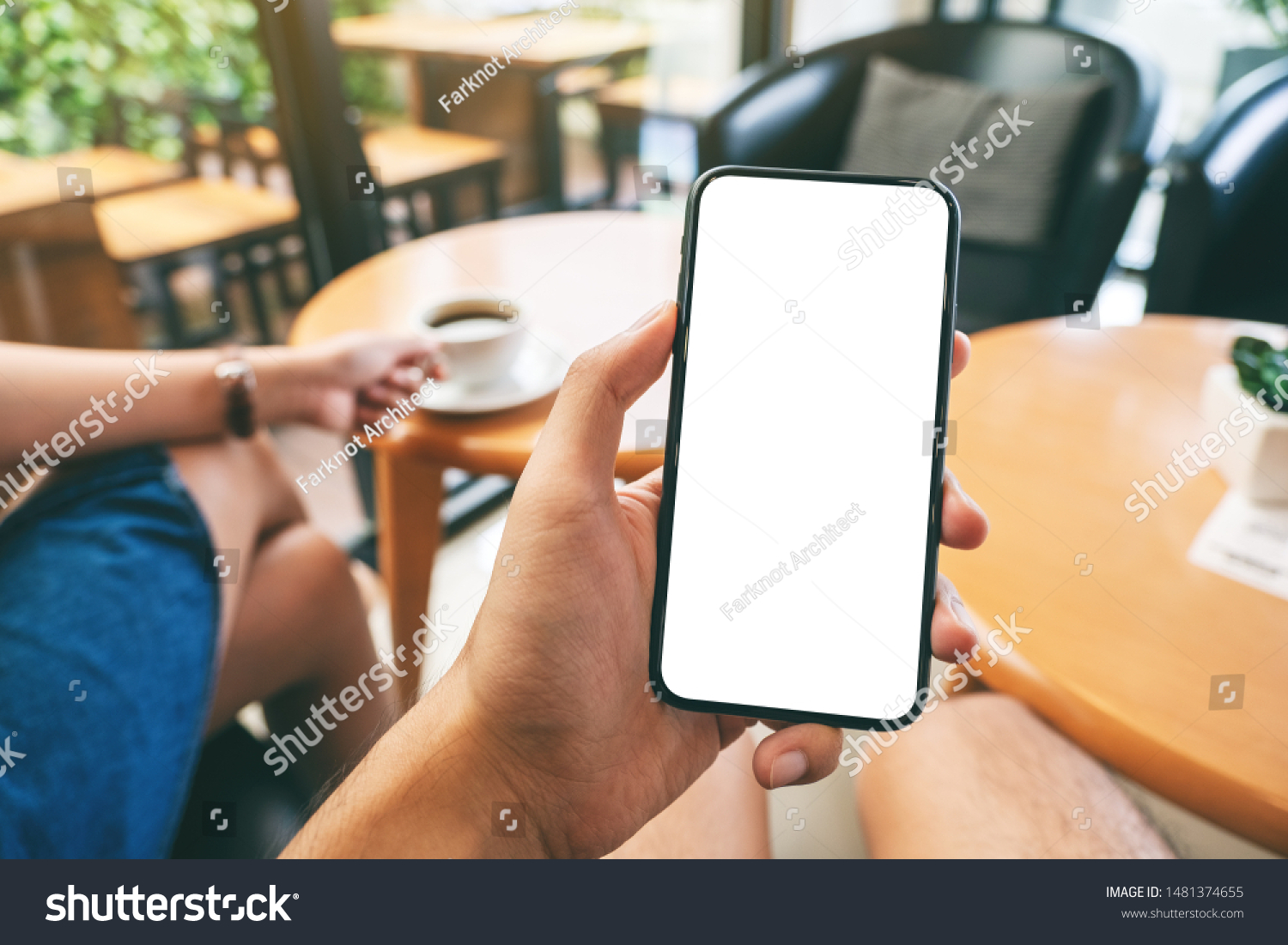 Mockup image of a man's hand holding black mobile phone with blank white screen with woman drinking coffee in cafe #1481374655