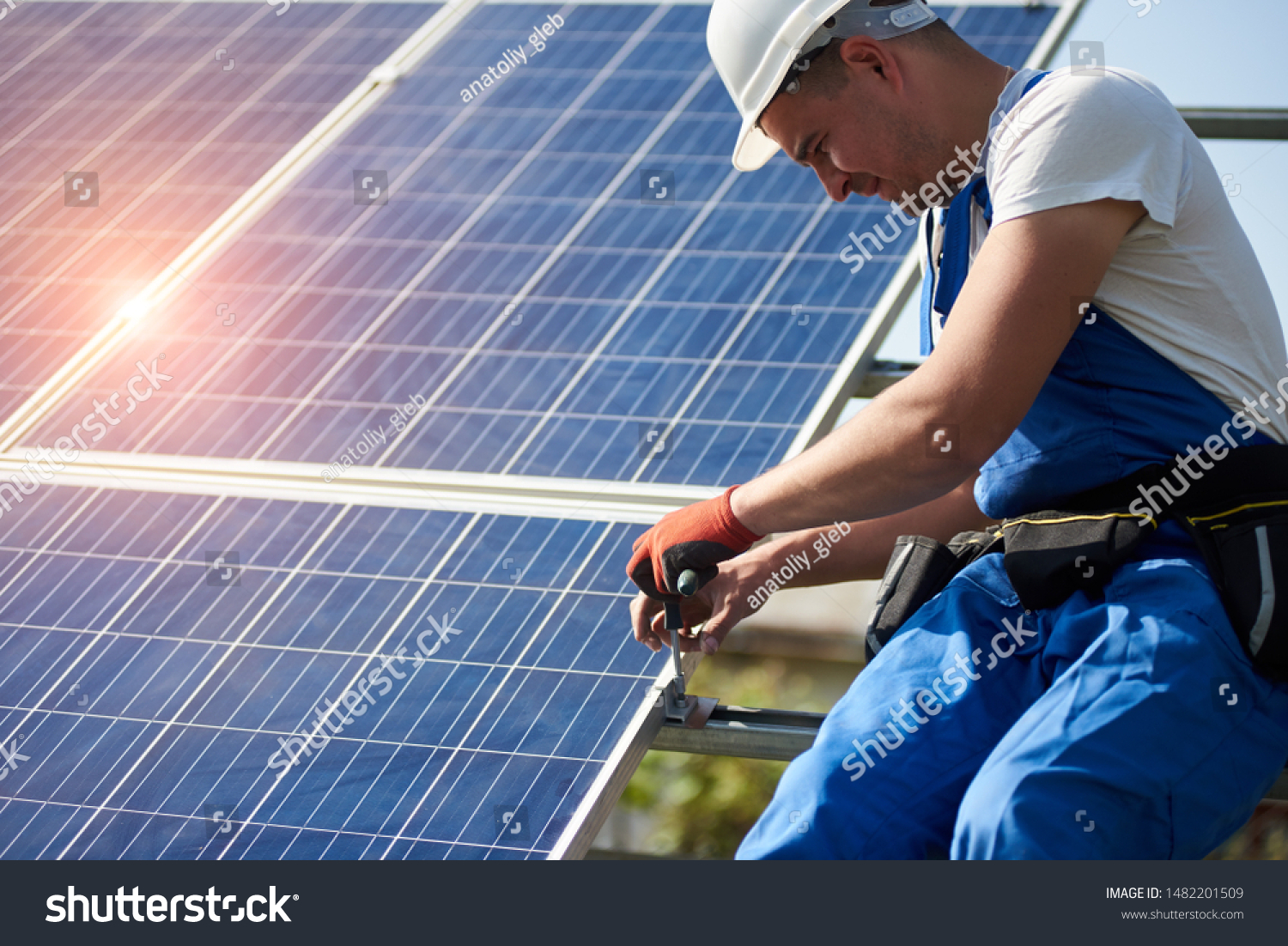 Professional technician connecting solar photo voltaic panel to metal platform using screwdriver. Stand-alone solar panel system installation, efficiency and professionalism concept. #1482201509