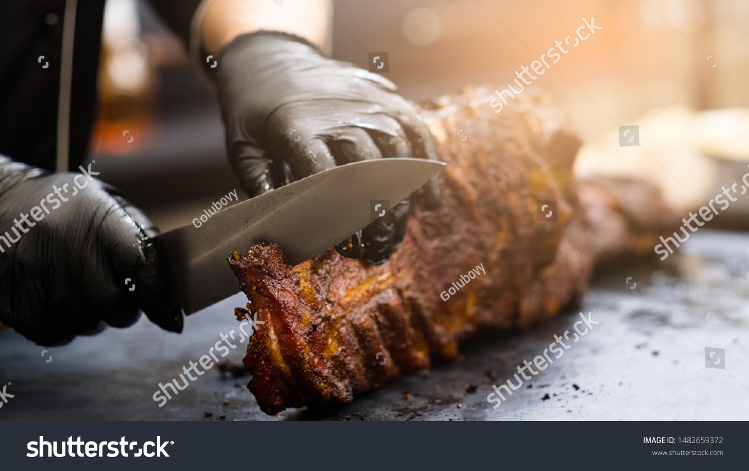 Grill restaurant kitchen. Chef in black cooking gloves using knife to cut smoked pork ribs. #1482659372