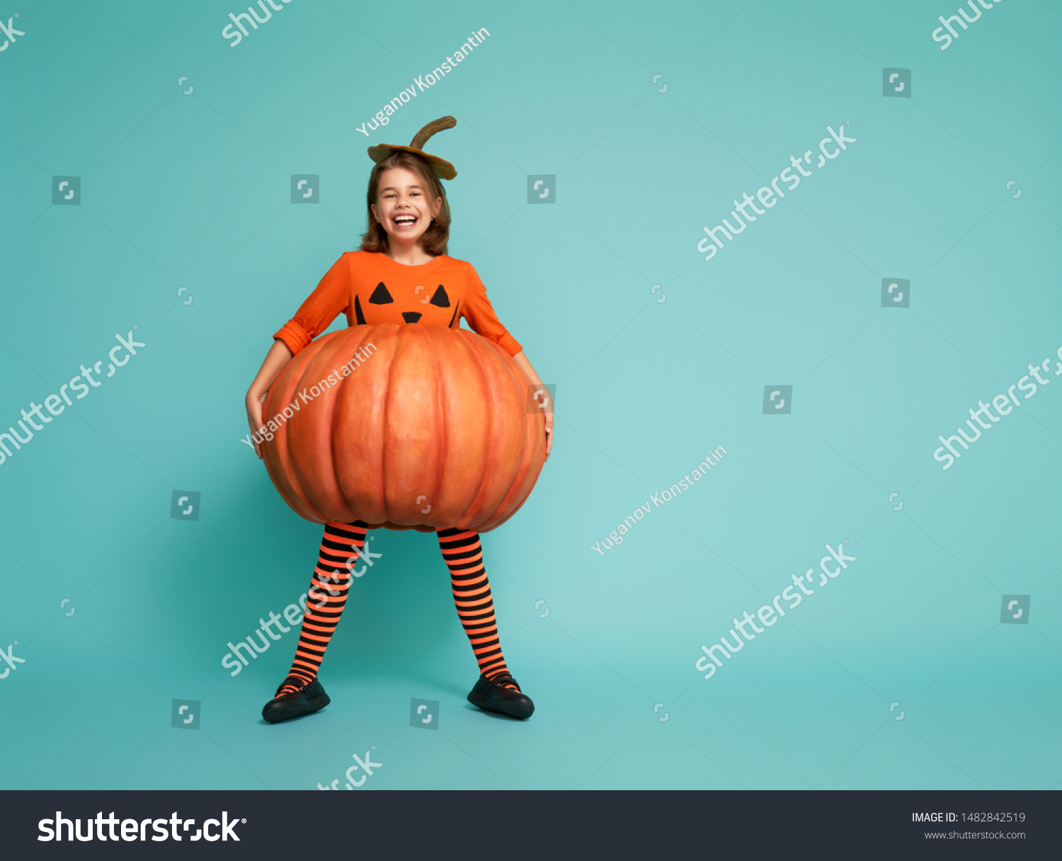 Happy Halloween! Cute little girl in pumpkin costume on turquoise background. #1482842519