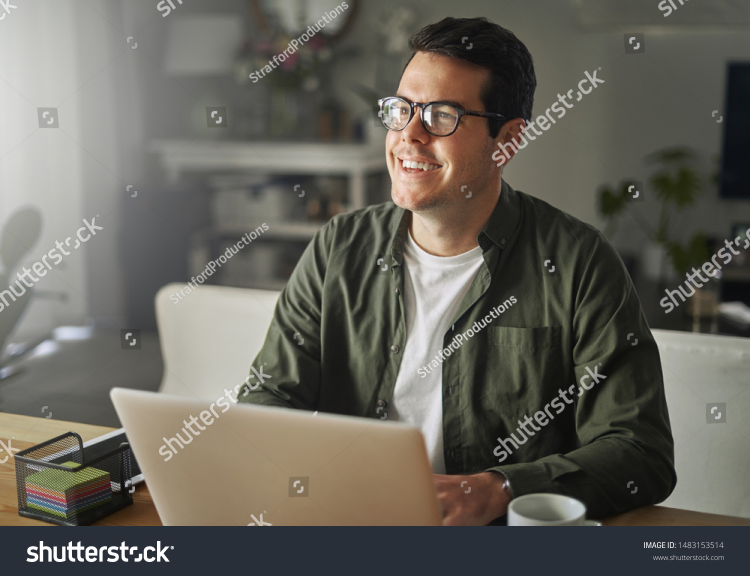 Smiling man with laptop sitting at desk looking away #1483153514