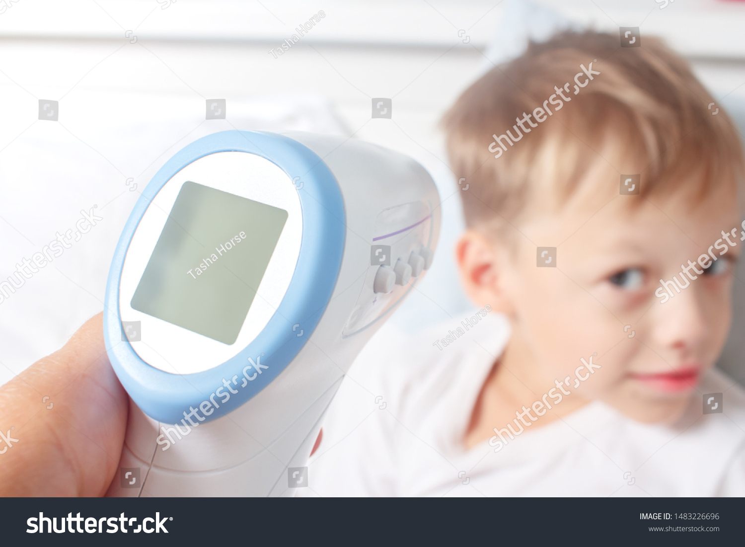 
Non-contact digital infrared thermometer in the hands of the mother of a sick boy. Monitoring and measuring the temperature of colds and flu. 
Cold season concept. #1483226696