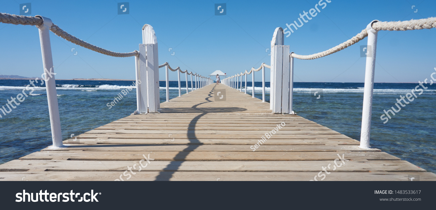 Pier on the seashore, with a girl walking along the pier into the distance. Travel.         #1483533617