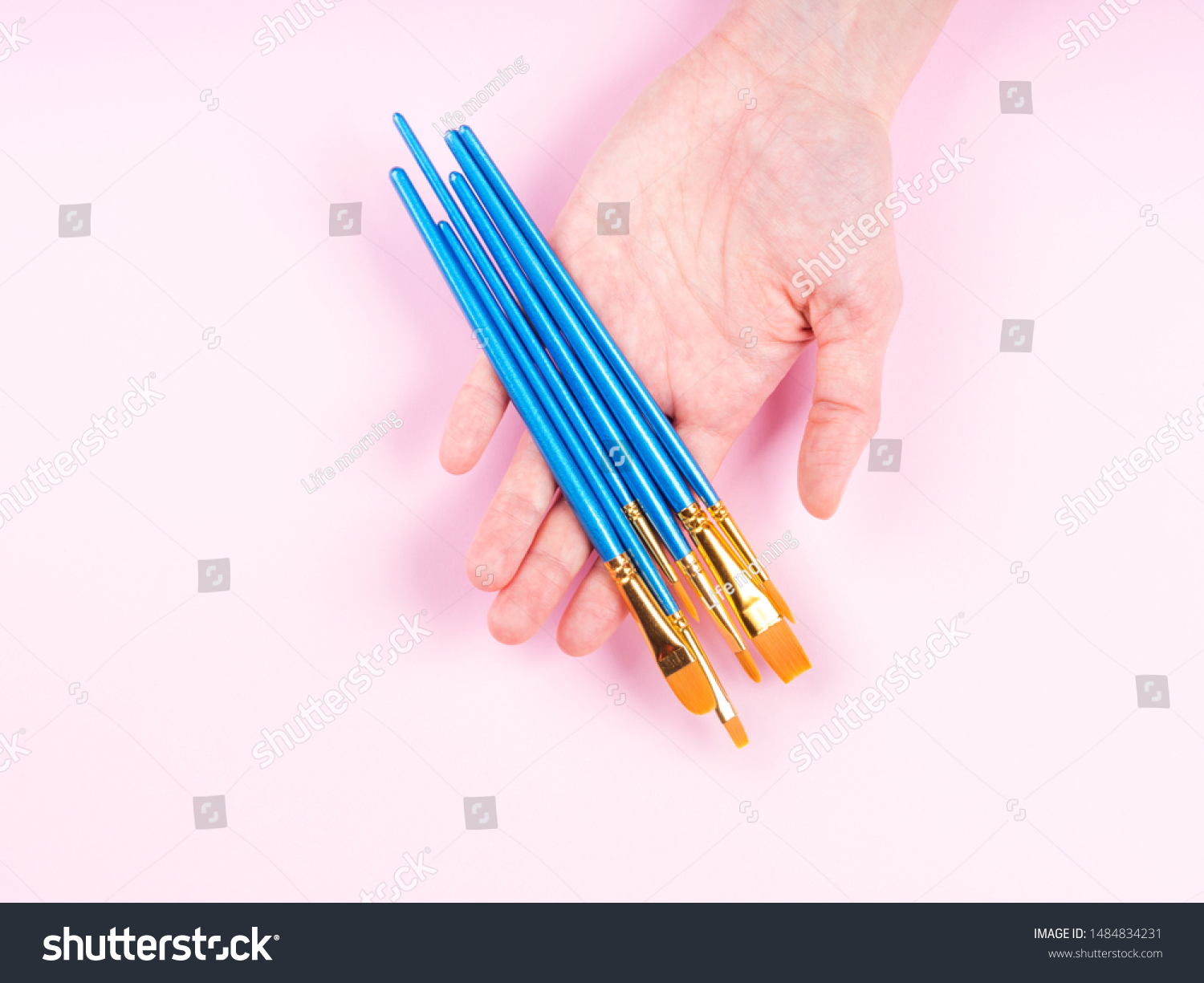 Blue paintbrushes in woman's hand on pink background. Art supply, art school education concept #1484834231