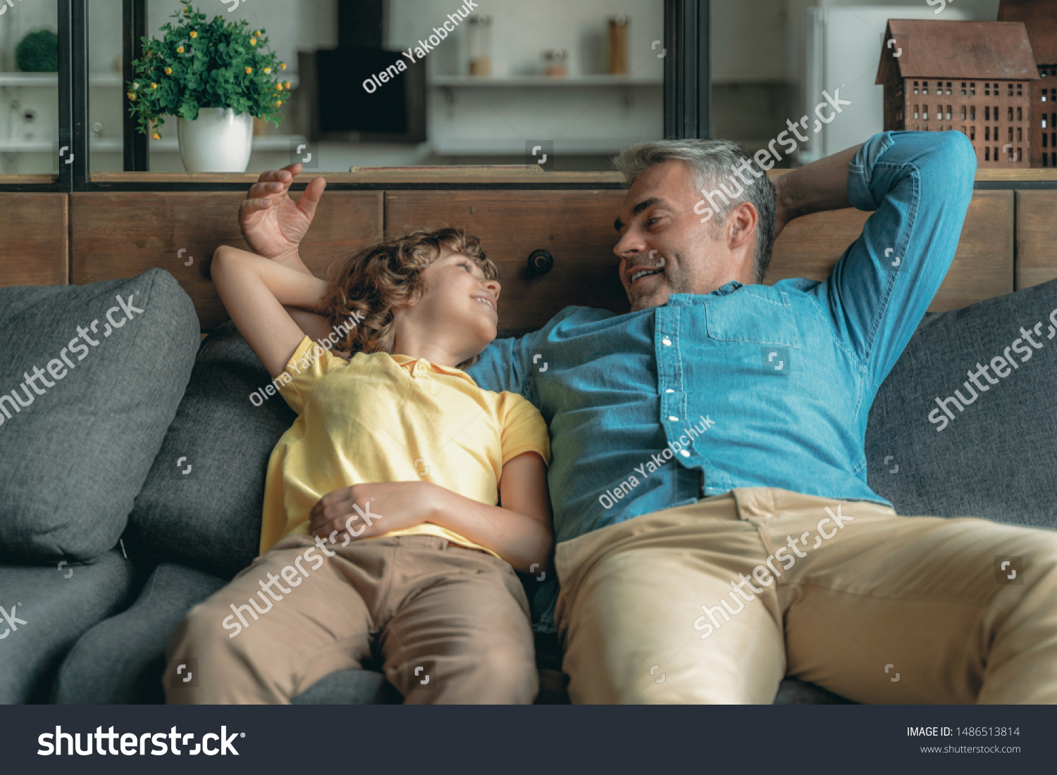Cheerful mature father spending day together with little son and sitting on couch #1486513814