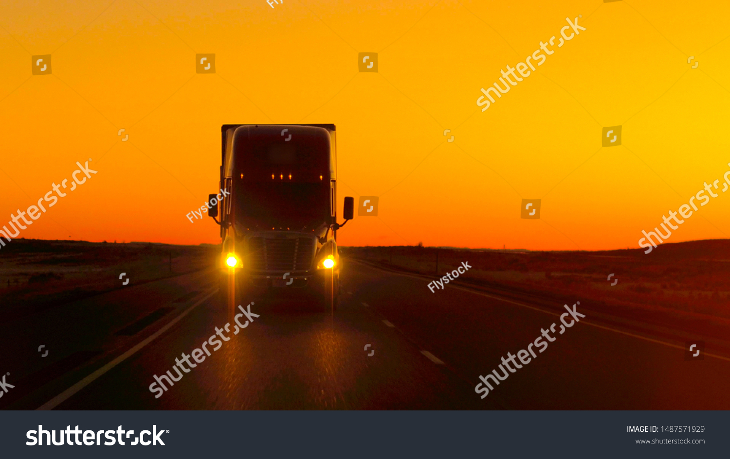 CLOSE UP LENS FLARE: Semi truck driving and hauling goods on empty highway across the Great Plains in golden morning. Freight delivery truck transporting cargo on interstate freeway at stunning sunset #1487571929