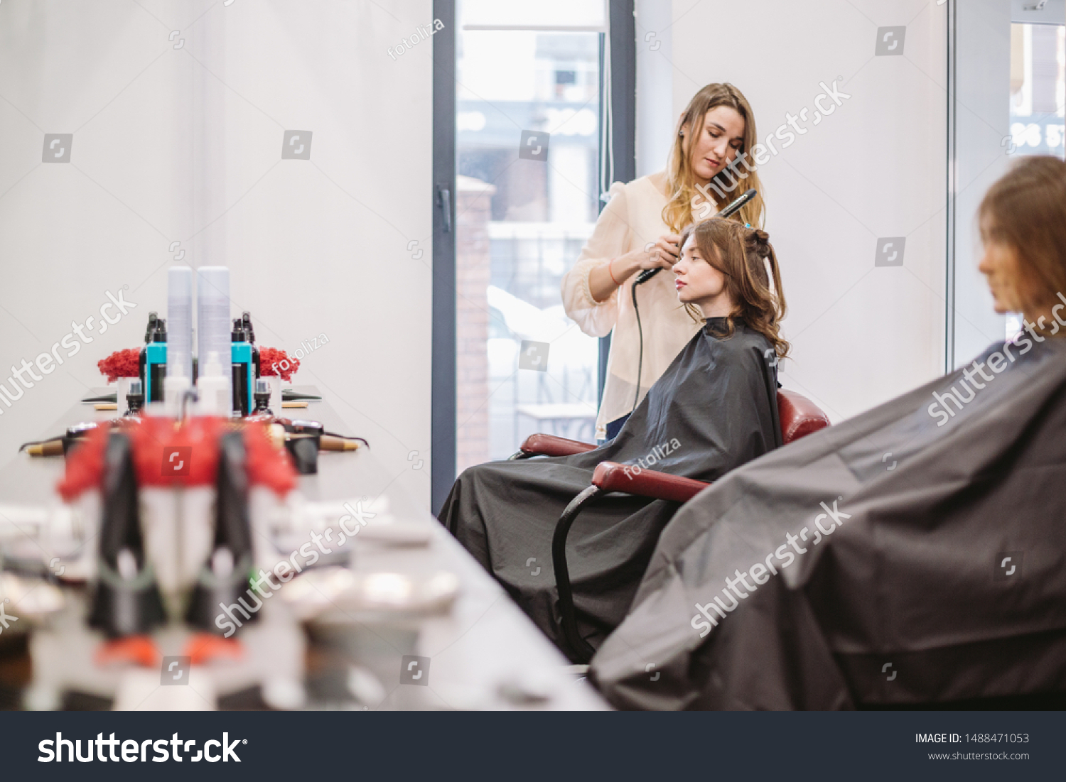 beauty, hairstyle concept, happy young woman and hairdresser with hair iron making hairdo at hair salon. Woman Having Hair Stylized Hairdresser. Smoothes Hair Curling. Stylist Using Tool for Modeling. #1488471053