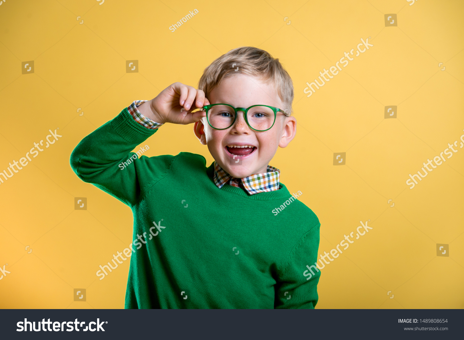 Portrait of blond little boy in green sweater and glasses. Kid at eye sight test. Stylish child holding glasses and looking at camera. Vision, eyesight measurement for school children. Back to school. #1489808654