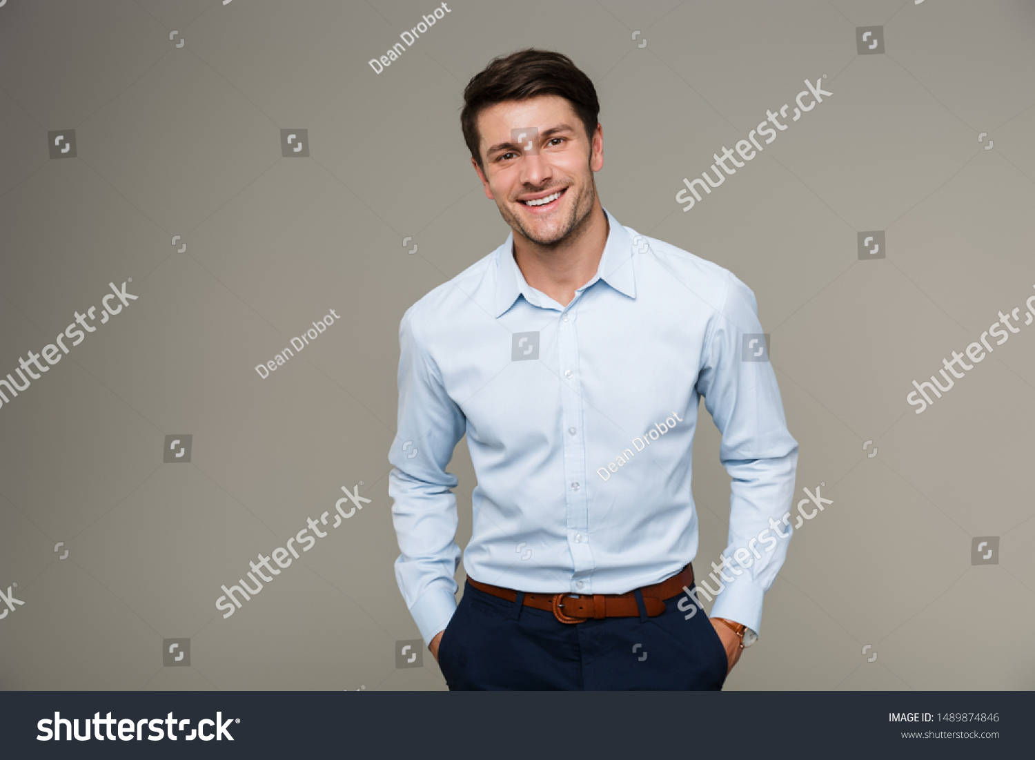 Image of happy brunette man wearing formal clothes smiling at camera with hands in pockets isolated over gray background #1489874846
